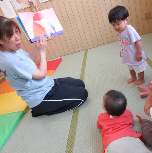 先生の絵本の読み聞かせを見る園児たち